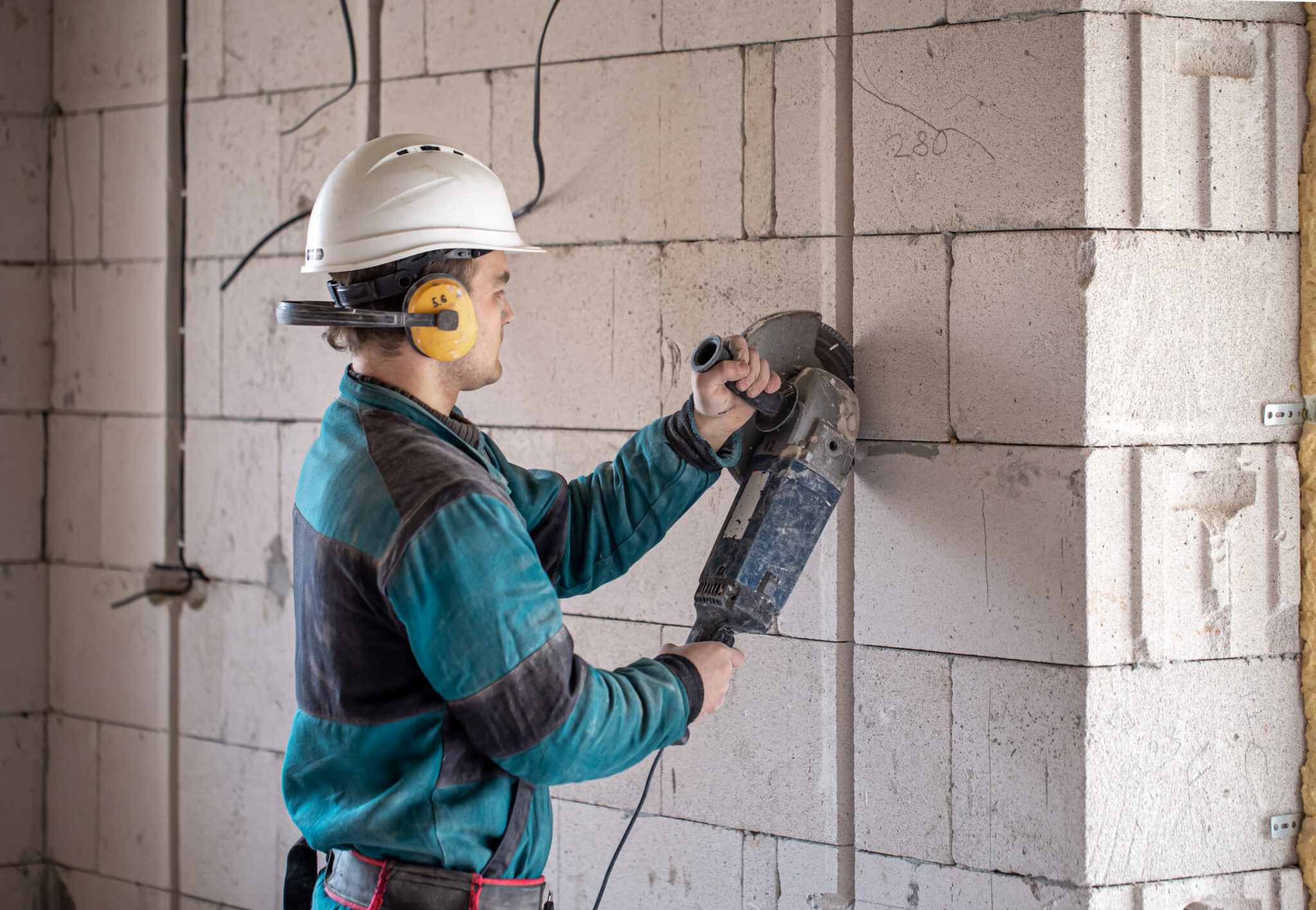 A professional builder in work clothes works with a cutting tool.